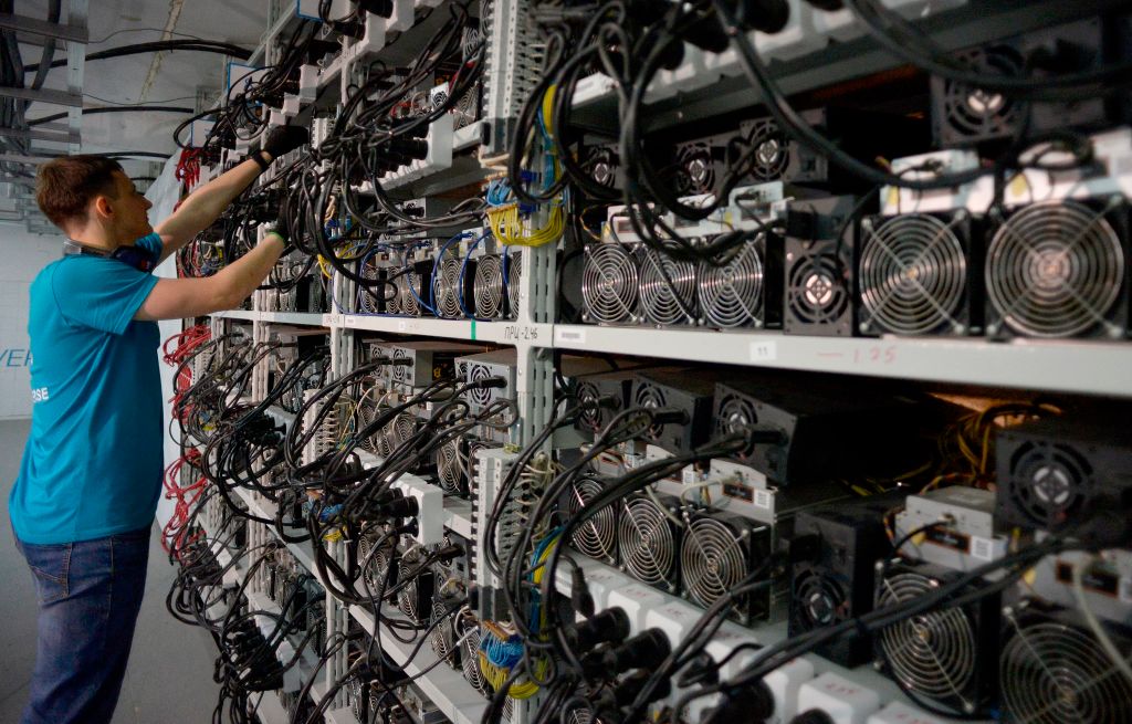 Technician maintains Bitcoin mining hardware with cooling fans in data center facility for AI infrastructure operations